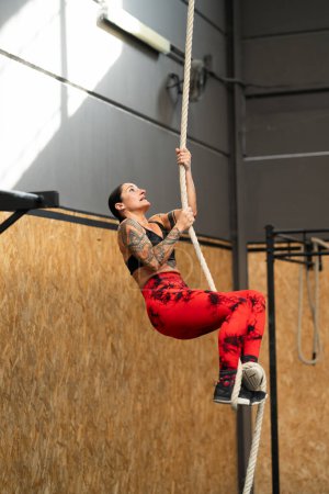 Photo for Vertical photo of a strong mature woman climbing a rope in a cross training gym - Royalty Free Image