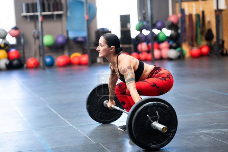 Téléchargez les photos : Vue latérale d'une femme sportive mature soulevant des poids dans la salle de gym - en image libre de droit