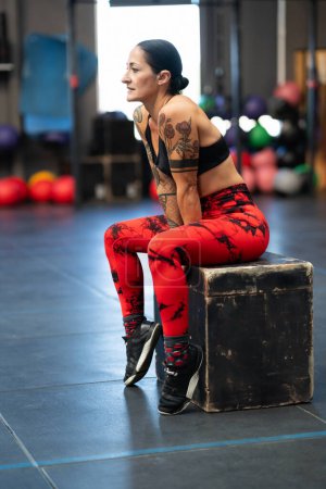 Photo for Vertical photo of a relaxed mature sportswoman sitting on a box in the gym - Royalty Free Image