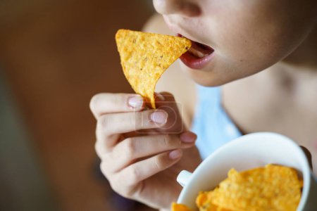 Téléchargez les photos : D'en haut de la récolte adolescent méconnaissable manger délicieuse puce nacho mexicaine à la maison - en image libre de droit