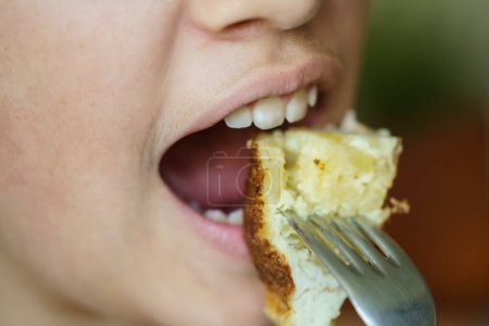Photo for Closeup of crop anonymous young girl eating delicious potato omelette from fork at home - Royalty Free Image