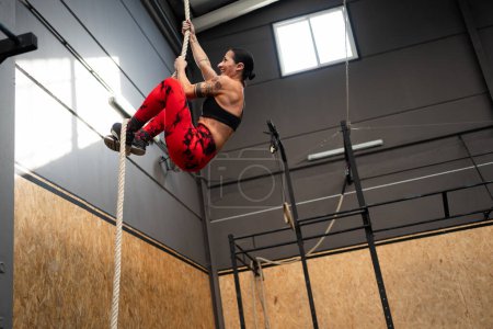 Photo for Low angle view photo with copy space of a fit mature woman climbing a rope in a cross training gym - Royalty Free Image