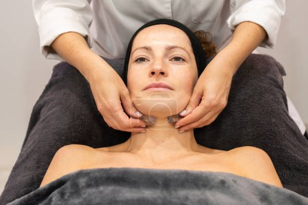 Téléchargez les photos : Angle élevé de culture cosmétique anonyme massant le cou de la femme avec des cristaux pendant la procédure de rajeunissement en clinique de beauté - en image libre de droit