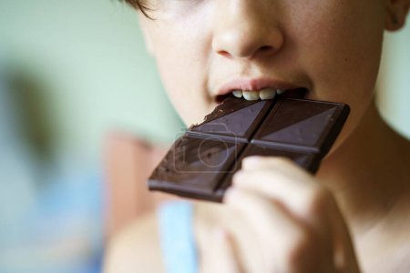 Gros plan d'adolescente méconnaissable mangeant de délicieuses barres de chocolat à la maison