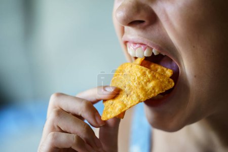 Photo for Closeup of crop anonymous teenage girl with mouth wide open about to eat spicy nacho chips at home - Royalty Free Image