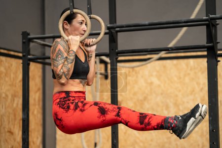 Mujer madura fuerte colgando de anillos olímpicos mientras hace ejercicio en un gimnasio