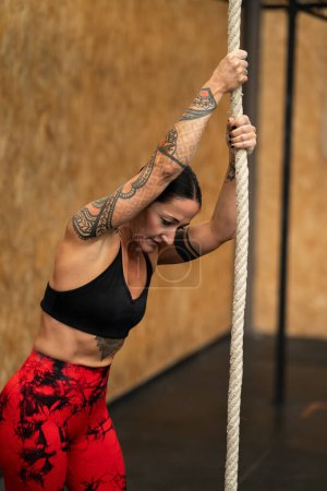 Téléchargez les photos : Femme sportive fatiguée sur le point de grimper une corde dans une salle de gym - en image libre de droit