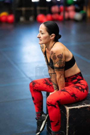Photo for Vertical photo of a mature fit woman sitting on a box resting after training in a gym - Royalty Free Image