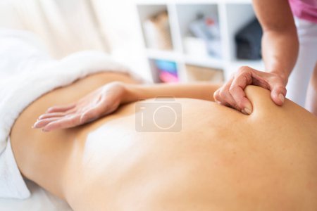 Photo for From above of crop anonymous female therapist massaging shoulder blade of patient lying on stomach with arm on back during physiotherapy session in modern clinic - Royalty Free Image