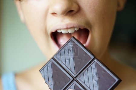 Photo for Closeup of crop anonymous teenage girl with mouth wide open about to eat chocolate bar at home - Royalty Free Image