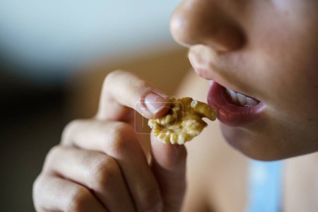 Photo for From above closeup of crop anonymous teenage girl eating healthy walnut kernel at home - Royalty Free Image