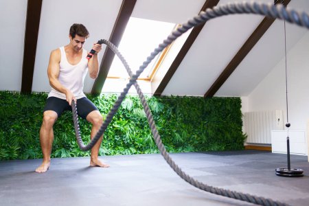 Photo for Full body of young fit male athlete in sportswear exercising with battle ropes while improving core strength power and endurance in modern gym - Royalty Free Image