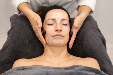 Photo for High angle of crop anonymous female cosmetician massaging cheeks of woman with natural crystals while smoothing facial skin - Royalty Free Image