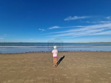 Photo for Girl with hat in front of the sea, on a sandy beach. Valdelagrana Beach in Puerto de Santa Maria, Cadiz, Andalusia, Spain - Royalty Free Image