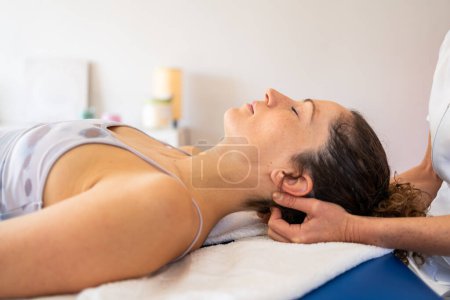 Photo for Patient lying face up in bed eyes closed while having back of head massaged by unrecognizable osteopath during rehabilitation in clinic - Royalty Free Image