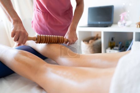 Téléchargez les photos : Cultivez une thérapeute anonyme qui fait un massage de thérapie du bois sur la jambe d'un patient allongé sur son lit pendant une séance de physiothérapie dans une clinique moderne - en image libre de droit