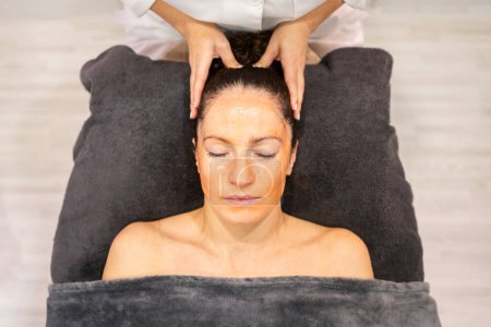 Photo for From above crop beauty specialist massaging head of female client lying on towel with closed eyes in beauty center during skin care treatment - Royalty Free Image