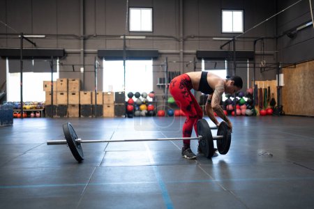 Horizontal photo with copy space of a mature fit woman preparing weights to dead-lifting in an empty gym
