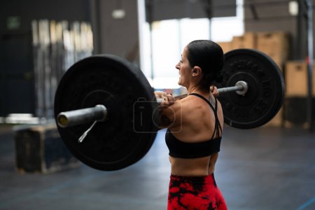 Photo for Rear view of a strong mature woman lifting weights in a gym - Royalty Free Image