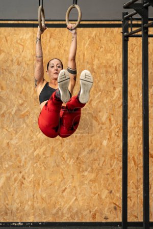 Téléchargez les photos : Photo verticale avec espace de copie d'une femme sportive mature faisant des exercices de base en utilisant l'anneau olympique dans un gymnase - en image libre de droit