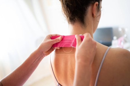 Photo for Back view of crop anonymous female receiving osteopathic and therapeutic treatment with kinesiology tape at back of neck while in modern clinic - Royalty Free Image