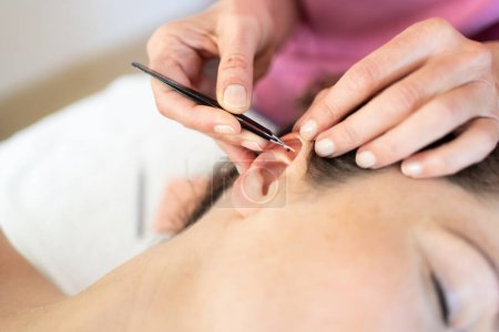 Photo for From above crop homeopath professional beautician applying auriculotherapy ear acupuncture techniques on woman client in modern clinic - Royalty Free Image