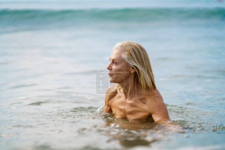 Foto de Mujer madura en buena forma bañándose en el mar. Anciana disfrutando de su retiro en un retiro junto al mar. - Imagen libre de derechos