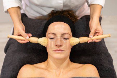 Foto de Cosecha esteticista utilizar cepillos para aplicar la crema facial en la cara de la joven cliente femenino en los centros de belleza durante la sesión cosmética y el cuidado de la piel - Imagen libre de derechos