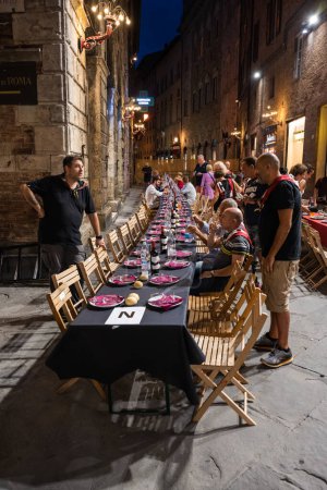 Photo for Siena, Italy - August 15 2022: The Grand Contrada Dinner of the Civetta or Little Owl Contrada on the Night before the Palio dell Assunta on Piazza Tolomei - Royalty Free Image