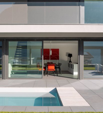 Foto de Villa exterior moderna con piscina. Ventanas abiertas y sala de estar minimalista. No hay nadie adentro - Imagen libre de derechos