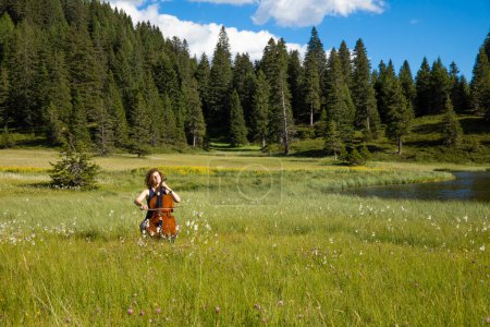 Photo for Woman plays the cello on a hot summer day in the middle of a meadow. Switzerland - Royalty Free Image