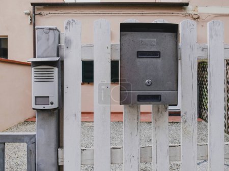 Photo for Mailbox with an intercom next to it hanging on the white wooden fence. Nobody inside - Royalty Free Image