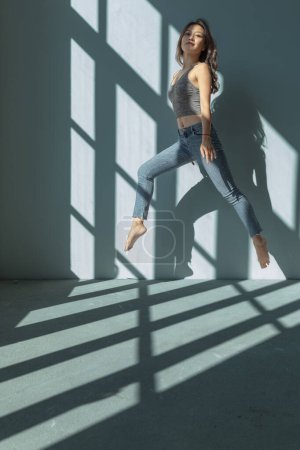 Photo for Asian dancer girl makes an acrobatic jump illuminated by the sun that enters through the window in an empty building. isolated - Royalty Free Image