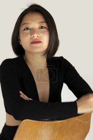 Foto de Joven hermosa china o asiática chica sentada en un vestido negro esu fondo blanco mientras mira directamente a la cámara. Hermoso retrato - Imagen libre de derechos