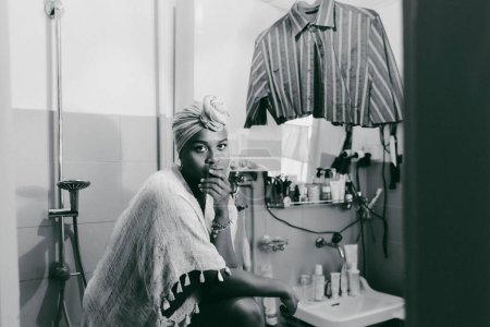 Foto de Retrato de una joven africana o una mujer de piel oscura, la mirada es penetrantemente significativa, la vida pasa y en el fondo cuelga una camisa - Imagen libre de derechos