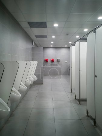 Photo for Large public pisshole with no one inside. A cold light accompanies it.  At the back attached to the bright red wall are two fans for drying hands. - Royalty Free Image