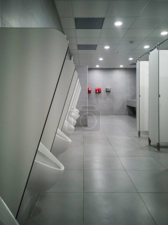 Photo for Large public pisshole with no one inside. A cold light accompanies it.  At the back attached to the bright red wall are two fans for drying hands. - Royalty Free Image