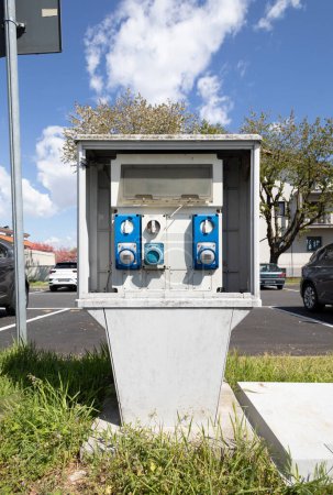 Photo for Small outdoor column in a public car park for electricity. in front of it and at its feet a little grass. it is summer the sky is blue and even a cloud is visible. - Royalty Free Image