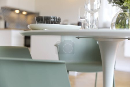 Téléchargez les photos : Détail de chaise turquoise et table blanche avec vaisselle dessus. La cuisine est en arrière-plan. Personne à l'intérieur - en image libre de droit