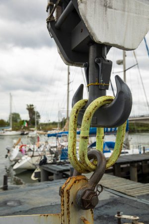 Téléchargez les photos : Détail d'un crochet attaché à une grue de construction dans un port en Italie. Ciel nuageux. Personne à l'intérieur - en image libre de droit