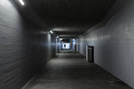 Long concrete pedestrian underpass passing under the train station in Melide, Switzerland. A man is walking in the background.