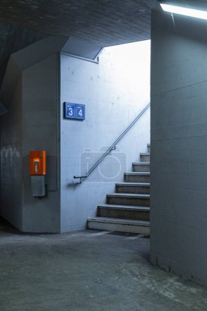 Foto de Detalle de una escalera en una estación de tren con la máquina de validación de billetes naranja junto a ella. Nadie dentro. - Imagen libre de derechos