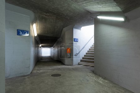 Foto de Corredor peatonal de hormigón bajo la estación de tren con la escalera y la máquina de validación naranja al lado. Nadie dentro. - Imagen libre de derechos