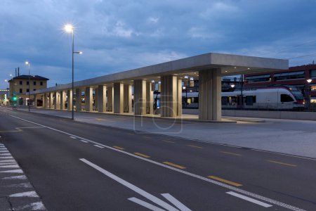 Foto de Moderno refugio de parada de autobús con la estación de tren detrás de él en Mendrisio. Infraestructura moderna en Suiza. No hay nadie adentro. - Imagen libre de derechos