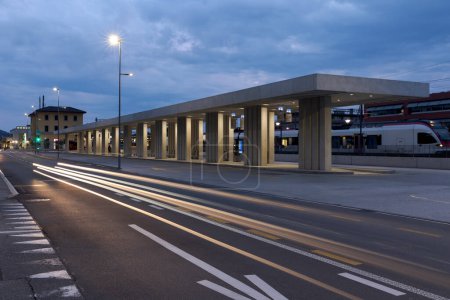 Moderno refugio de parada de autobús con la estación de tren detrás de él en Mendrisio. Infraestructura moderna en Suiza. No hay nadie adentro.