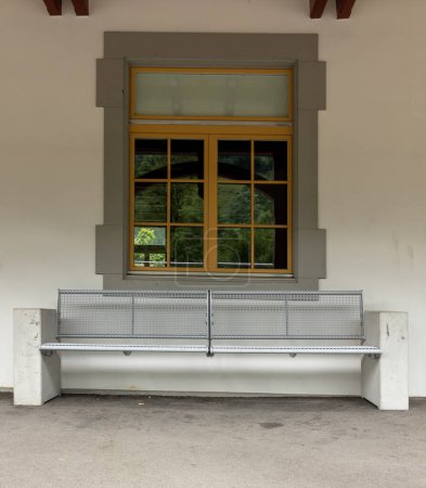 Foto de Banco frente a una ventana en una estación de tren suiza. Nadie está sentado en él. - Imagen libre de derechos
