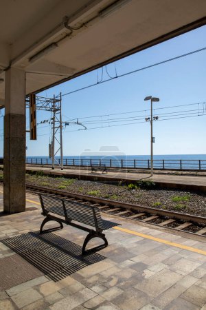 Foto de Las vías de la estación Devia Marina en Italia. Sin trenes, sin gente, completa desolación y tristeza. Hermosa vista al mar abierto, banco vacío - Imagen libre de derechos