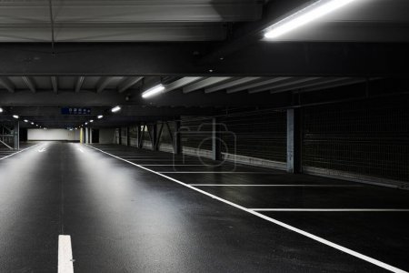 Photo for Modern underground garage with lamps illuminating the scene. Parking lines are drawn on the floor. No one inside - Royalty Free Image