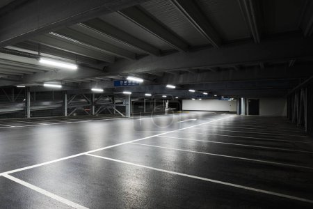 Téléchargez les photos : Garage souterrain moderne avec des lampes éclairant la scène. Des lignes de stationnement sont tracées sur le sol. Personne à l'intérieur - en image libre de droit