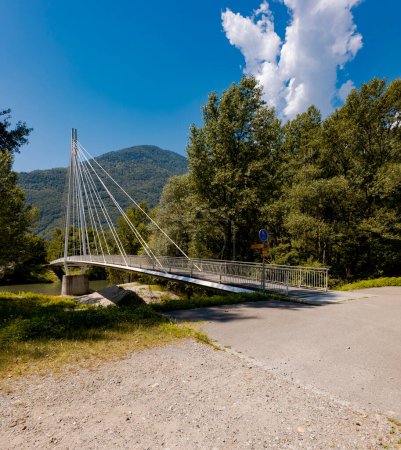 Photo for Modern pedestrian bridge in the middle of the mountains of Italian Switzerland, allowing you to cross the Ticino River. Beautiful sunny summer day. - Royalty Free Image